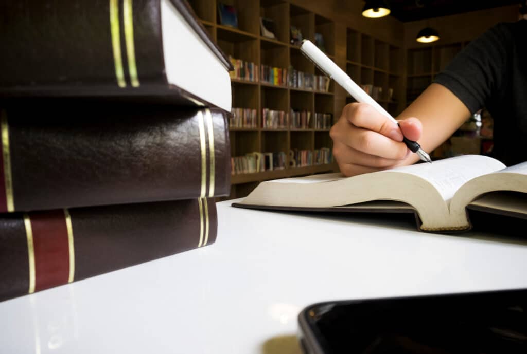 Woman reading book in library and taking notes