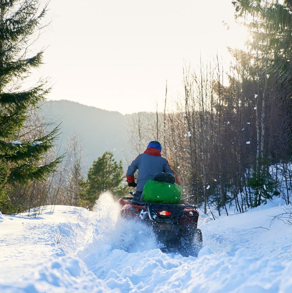 Rear view of a biker driving fourwheeler atv in winter in the mountains