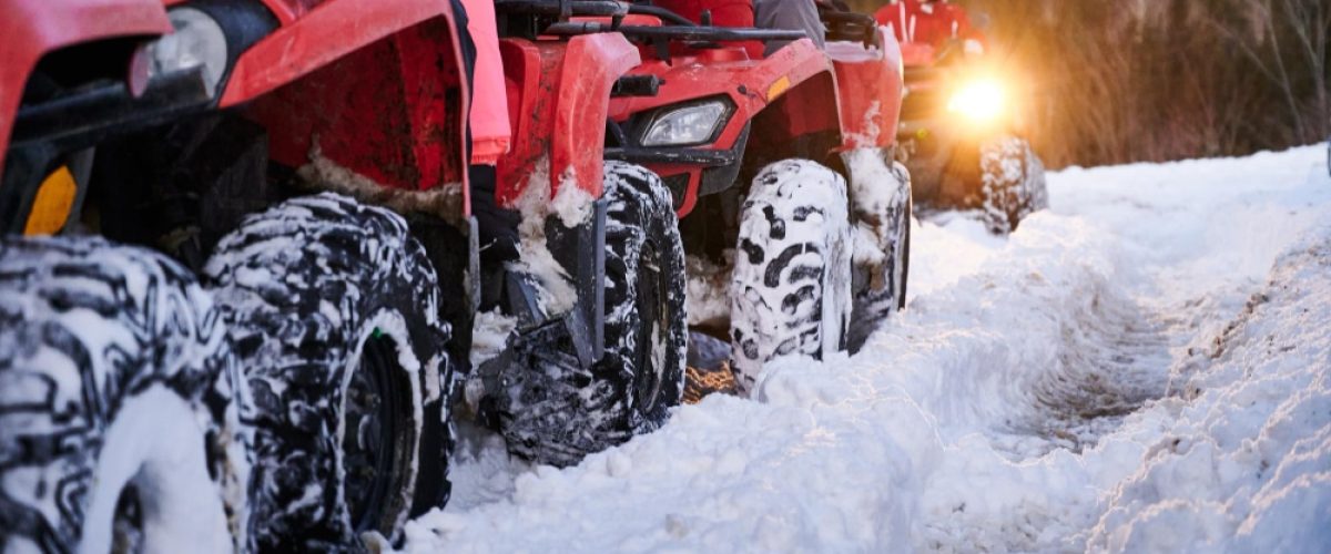 Group of people driving quad bikes on snowy road