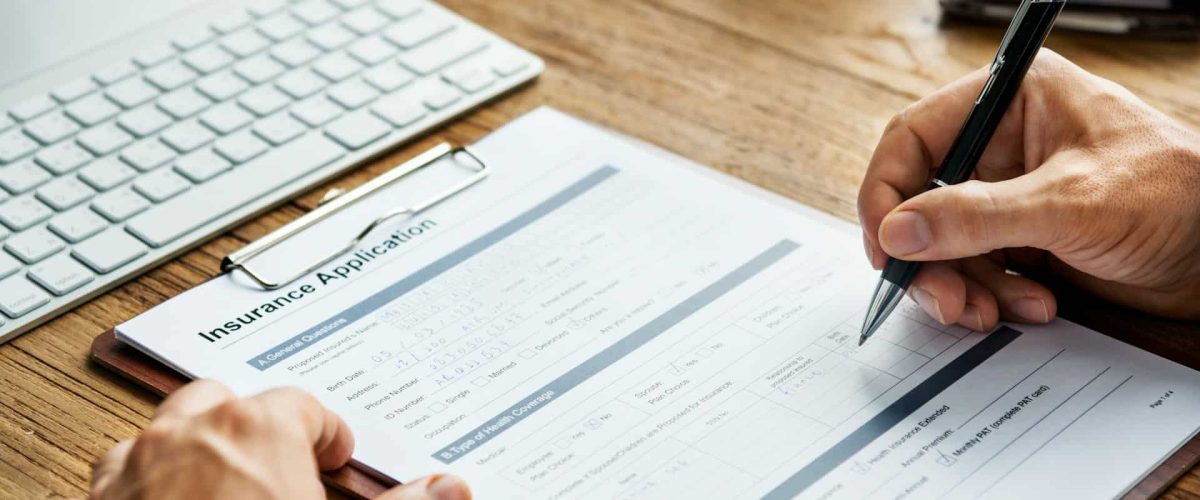 Image of an insurance form on a desk with hand holding a pen.