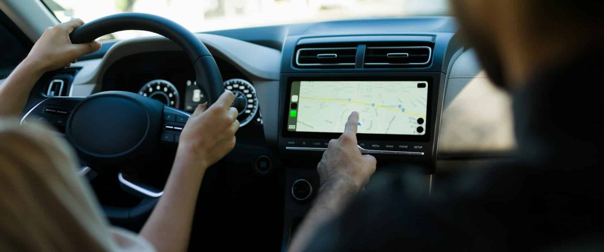 passenger man using the touch screen navigation panel in a car with a driver woman holding the steering wheel.