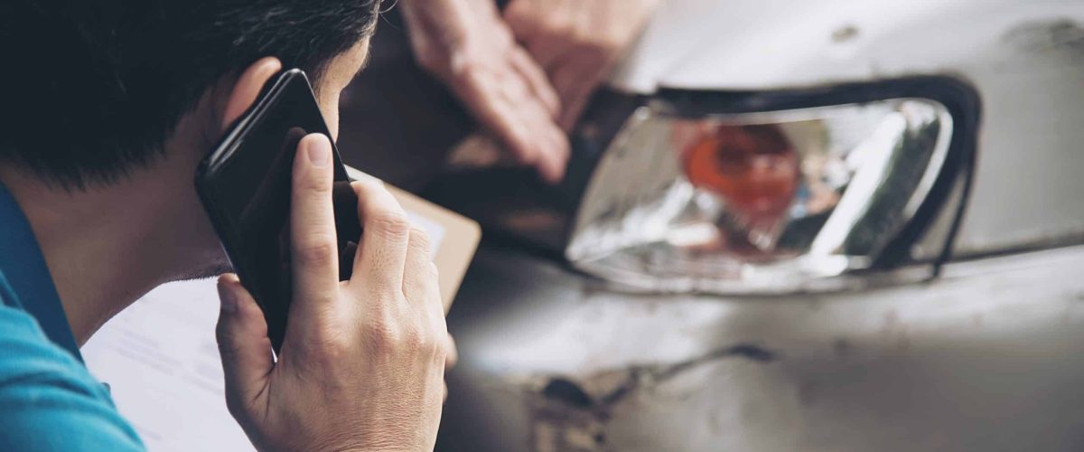 Man speaking on phone with in front of a car crash
